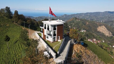 tepe üzerinde çok katlı villa, büyük türk bayrağı direği, taş istinat duvarları ve çay terasları; arka planda karadeniz manzarası (drone çekimi)