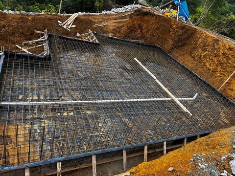 kazı çukurunda radye temel donatısı yakın plan; PVC tesisat boruları, bohçalama membranı ve kalıp payandaları