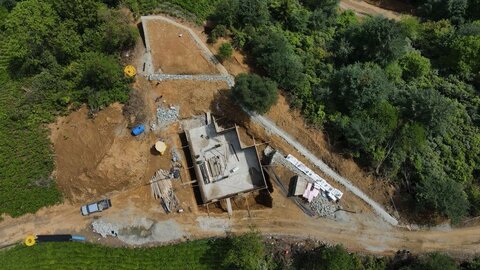 drone ile genel şantiye planı — dökülmüş temel, çevre istinat hatları, stok alanları ve erişim yolu