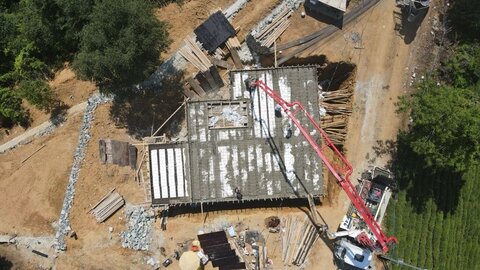 drone üstten — EPS bloklu döşeme üzerine beton dökümü; kırmızı pompa kolu ve şantiye ekipmanları