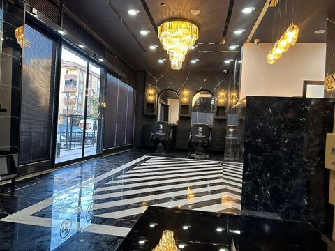 Salon genel görünüm — siyah mermer yüzeyler, çizgili zemin ve kademeli kristal avize; berber koltukları