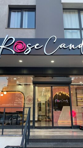 Rose Candy mağaza cephesi — geniş cam vitrin ve giriş kapısı, üstte aydınlatmalı logo tabelası