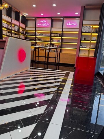 Neon ‘hello beautiful’ ve ‘shine’ yazılarıyla aydınlatılan ürün duvarı; zeminde diyagonal siyah-beyaz şeritler ve karşılama bankosu