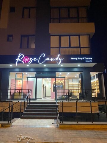 Gece görünümünde Rose Candy dış cephe — ışıklı tabela, cam vitrinler ve iç mekânın pembe/siyah detayları