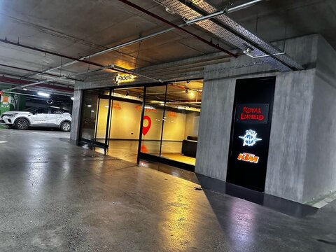 Otopark katında cam cepheli mağaza/servis girişi; sağda ışıklı totem panelde Royal Enfield, MV Agusta ve KTM logoları